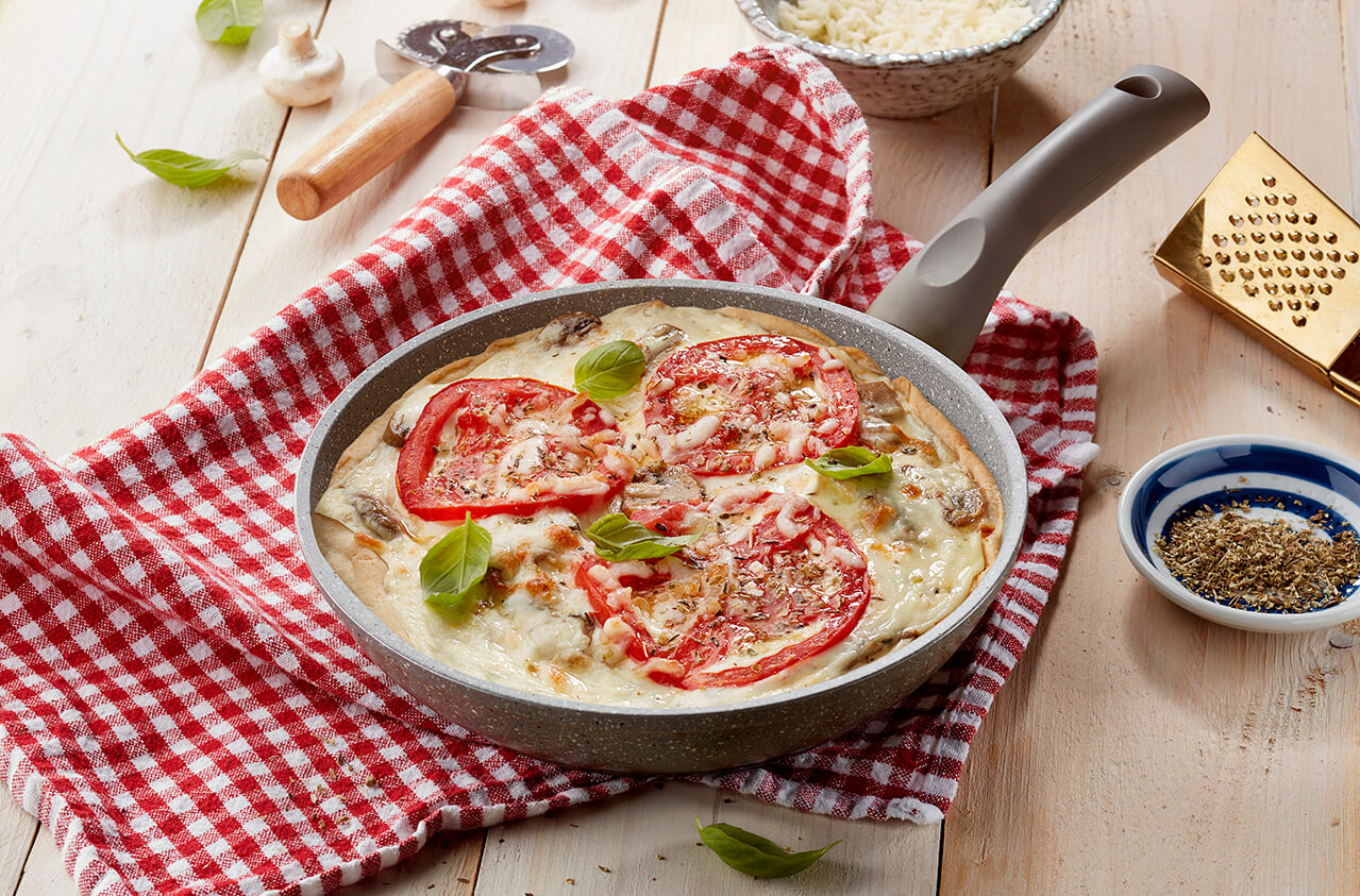 Cheese pizza in a pan with sautéed mushrooms and tomato rings sprinkled with oregano